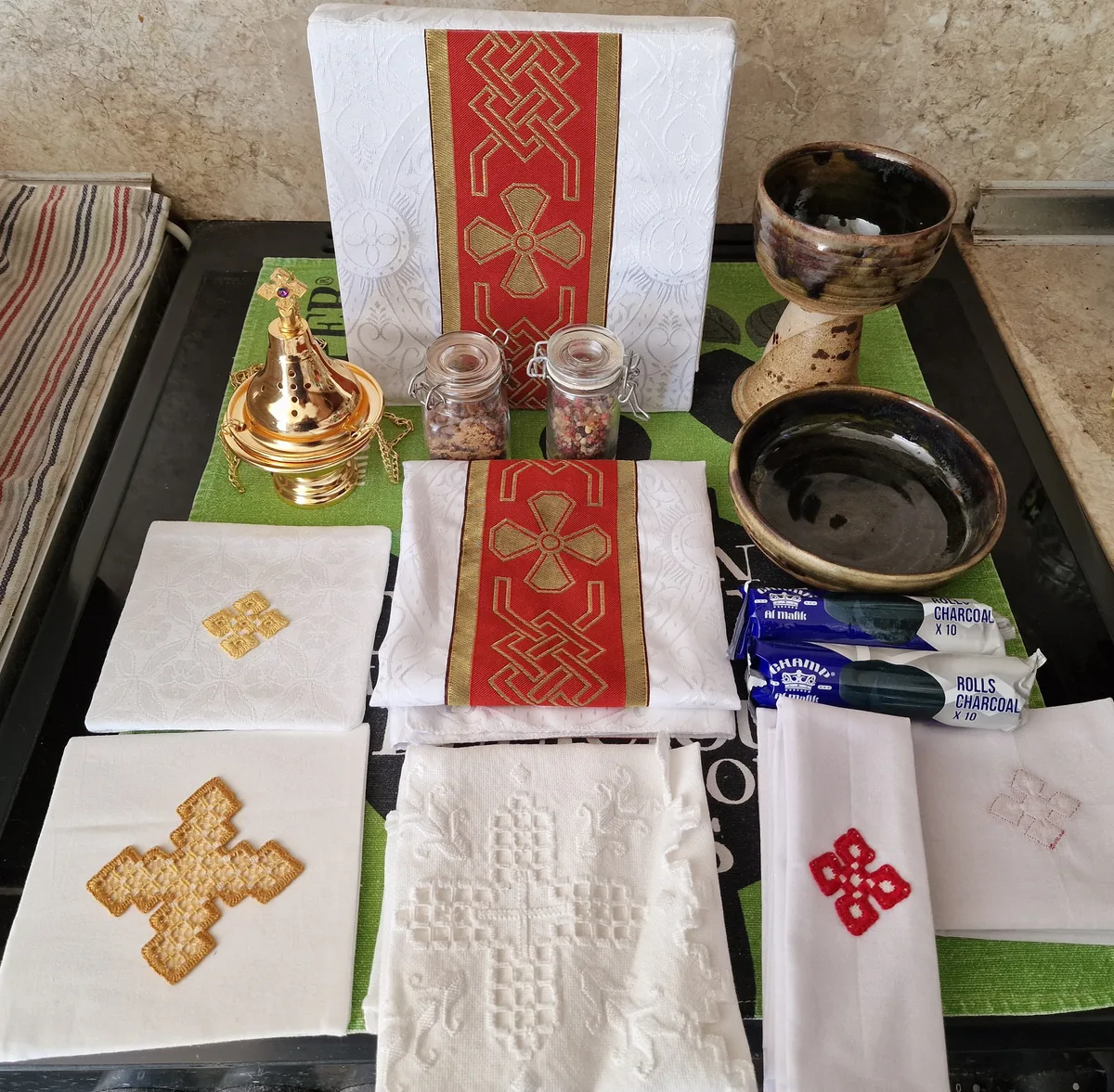 Embroidered white altar linens, red and gold fabric panels and jars of incense blends.