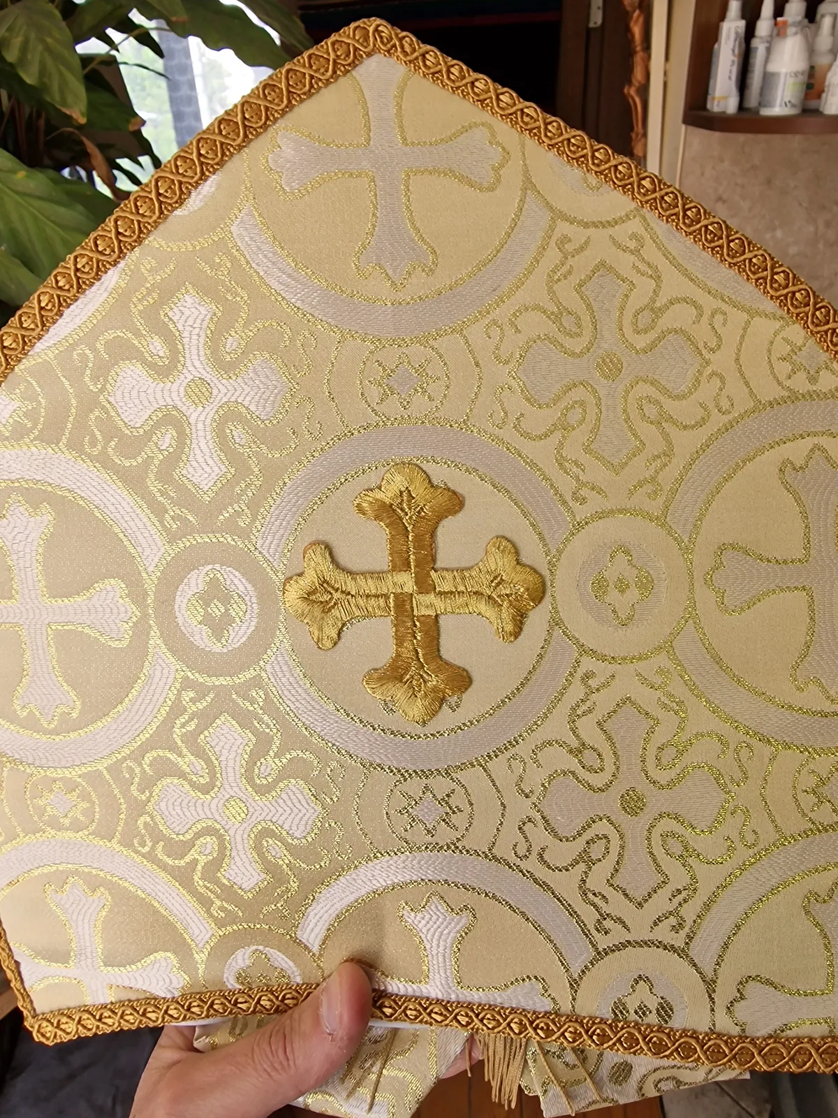 Close-up of a gold embroidered cross, patterned cream fabric and braided trim.
