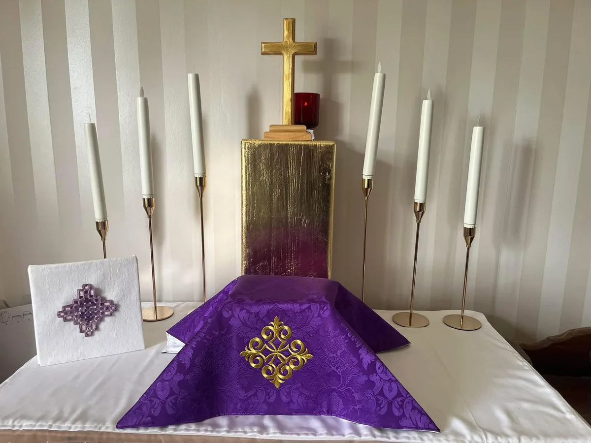 Purple liturgical textiles with gold embroidery and a white embroidered burse displayed on an altar.