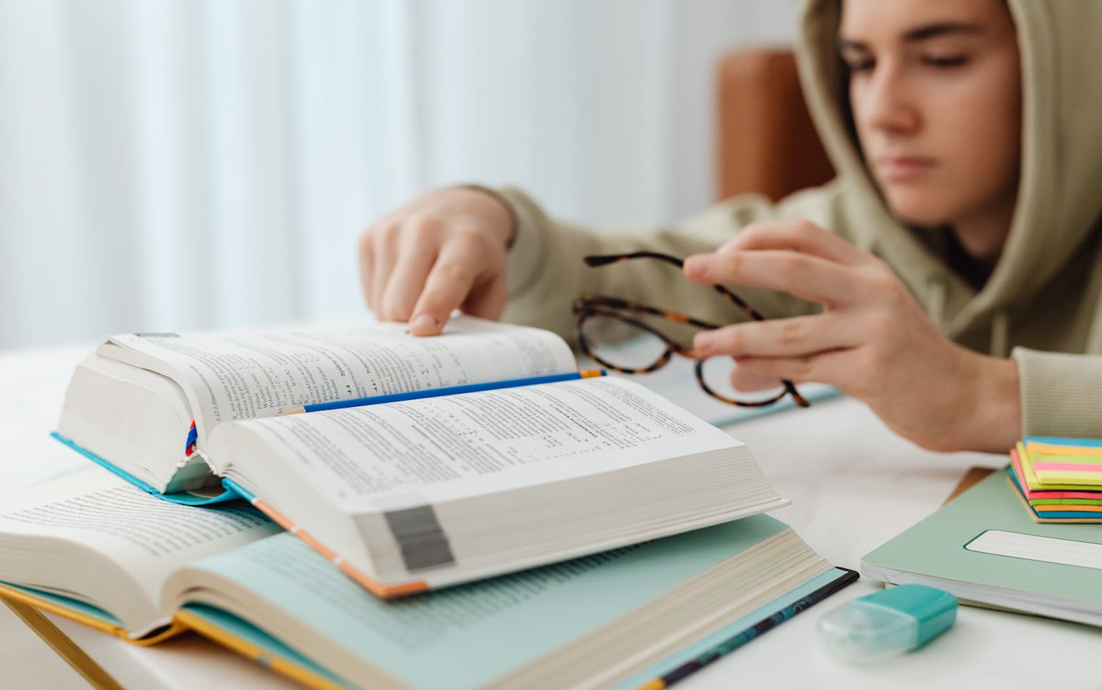 Focused teenager studying with open textbooks, eyeglasses, and notes.