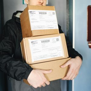 Courier carrying stacked cardboard packages for delivery service indoors.
